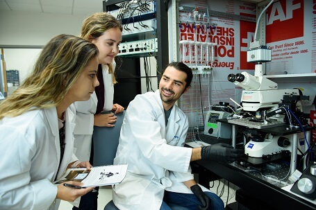 Three students working in a lab with a microscope