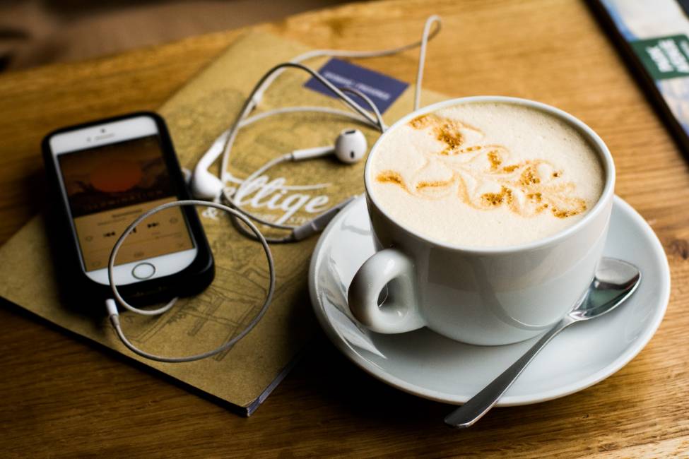 phone with plugged-in headphones next to a coffee cup