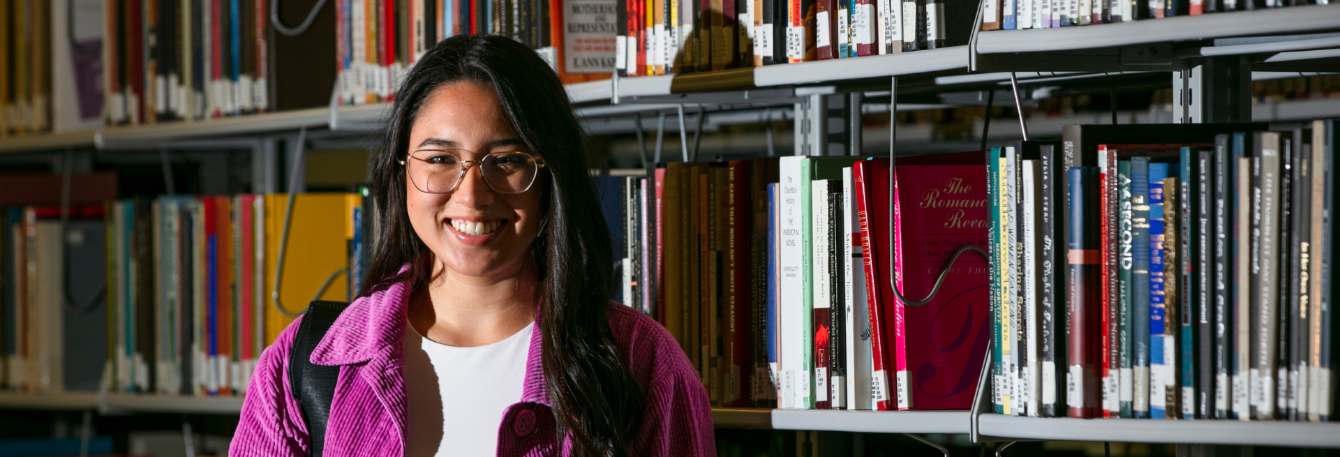 Student with glasses smilling in front of a bookshelf