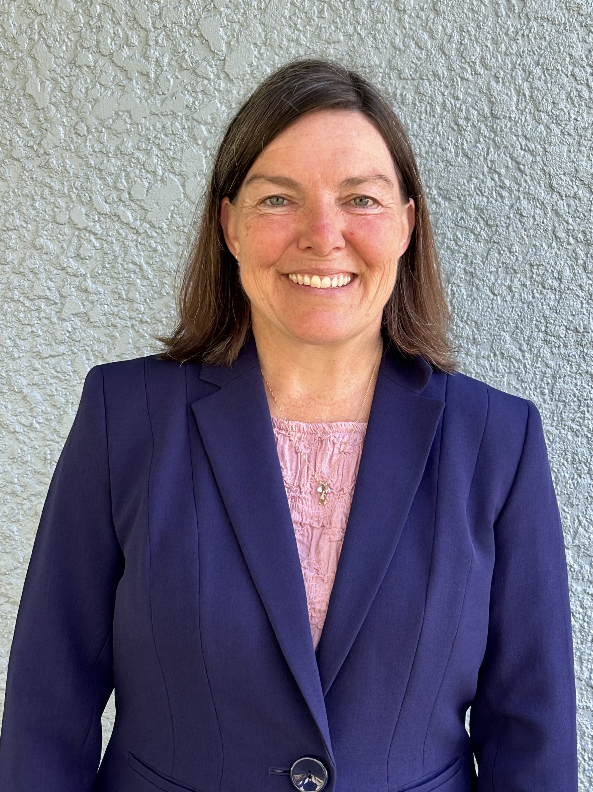 Faculty member in a blue blazer in front of a wall