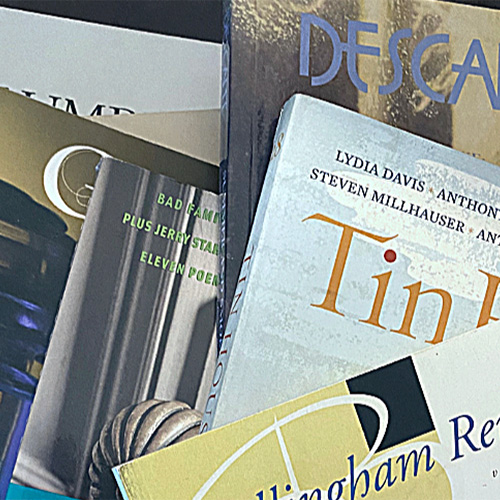 A close-up of a stack of books with visible spines, including poetry and literature titles, arranged slightly askew on a shelf.