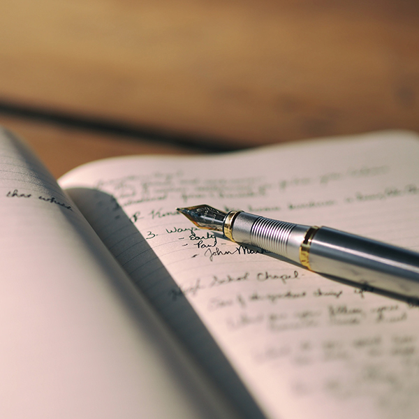 A fountain pen rests diagonally across an open lined notebook filled with handwritten notes.