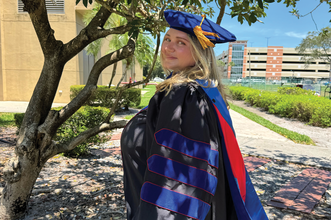 Cristina Pimenta in a cap and gown under a tree on the Florida Atlantic Boca campus