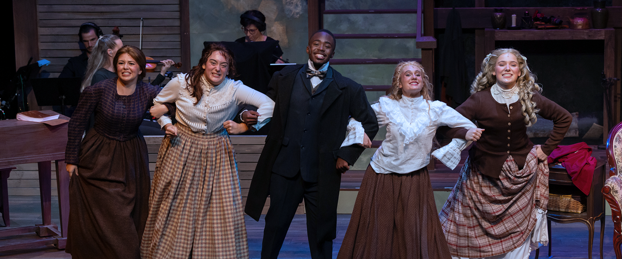 Actors on stage in costume smiling and holding hands