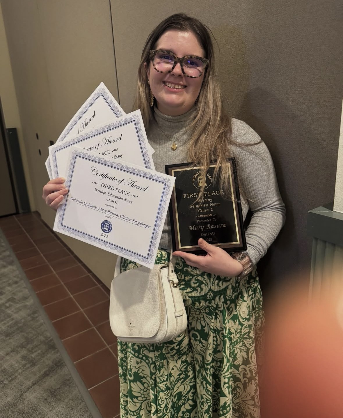 Graduate Student, Mary Rasura, holding up her multiple recognitions received at the Florida Press Club Awards