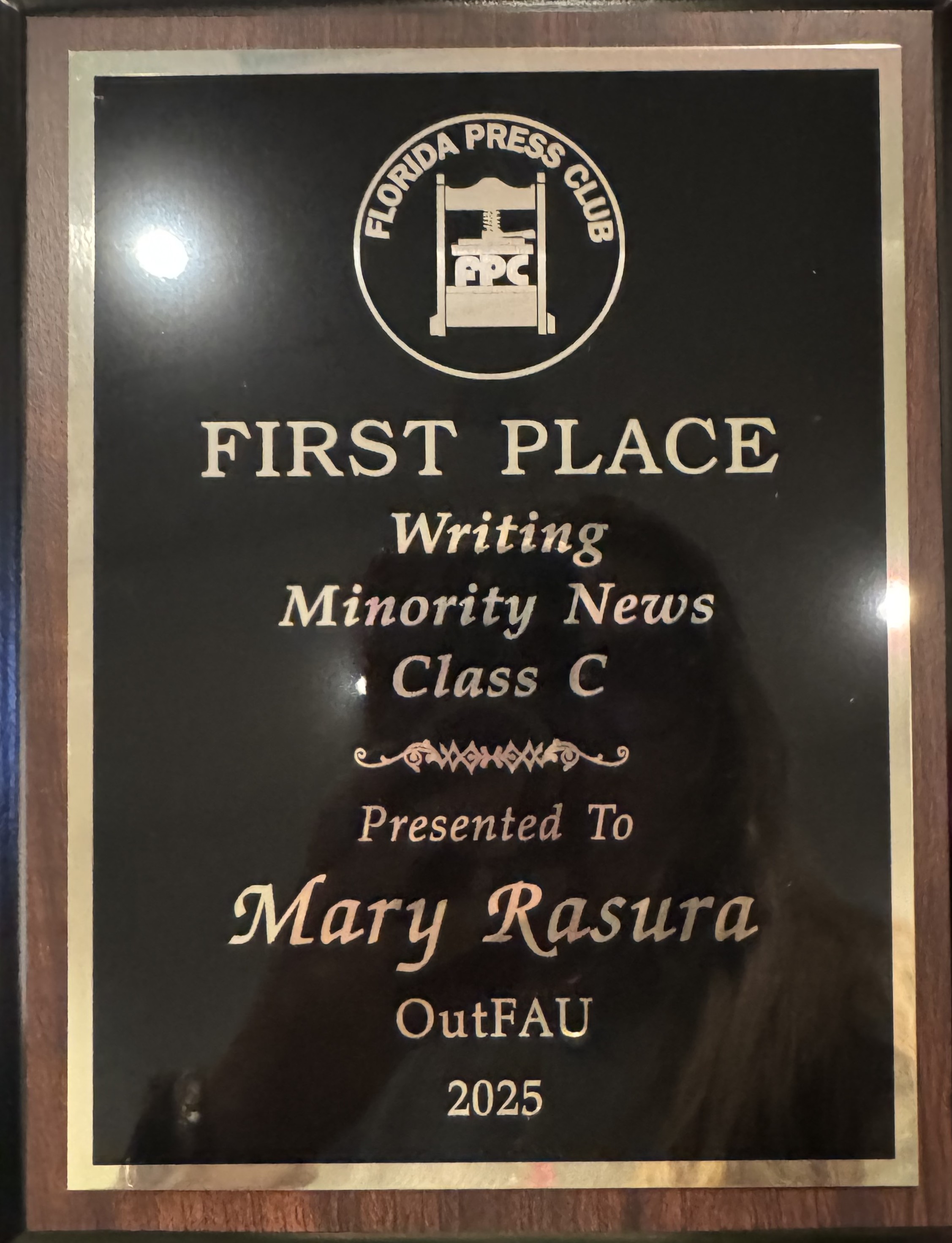 Details of plaque awarded to Mary Rasura "First Place Writing Minority News Class C Presented to Mary Rasura OutFAU 2025"