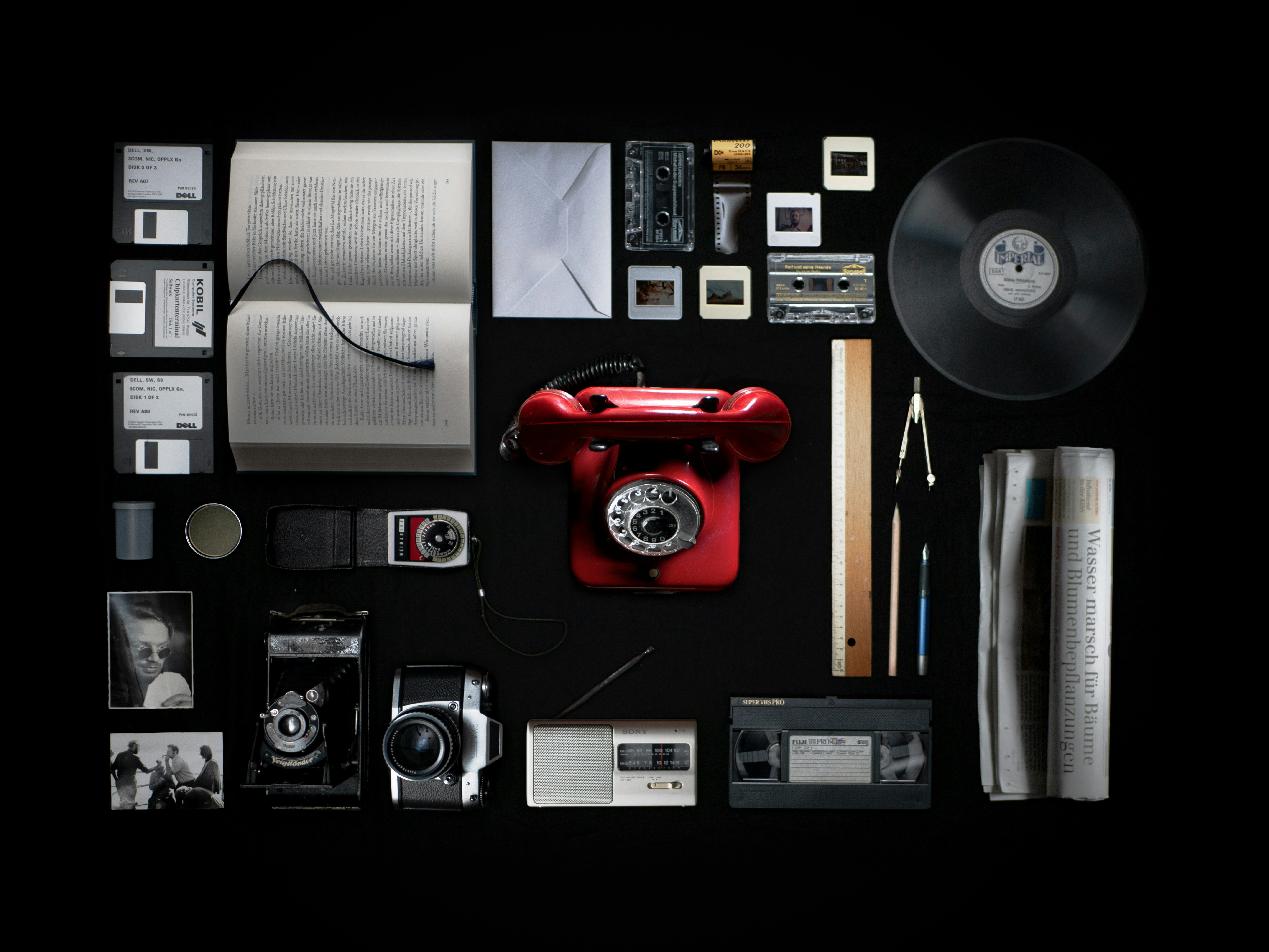 Image containing multiple versions of mass media such as cameras, photography, letters, tapes, hard drives, newpaper, film, and vinyl record.