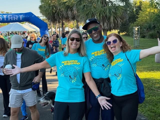 2 women and a man standing side by side smiling and wearing teal shirts that say 'Neuro Squad' in bright yellow.