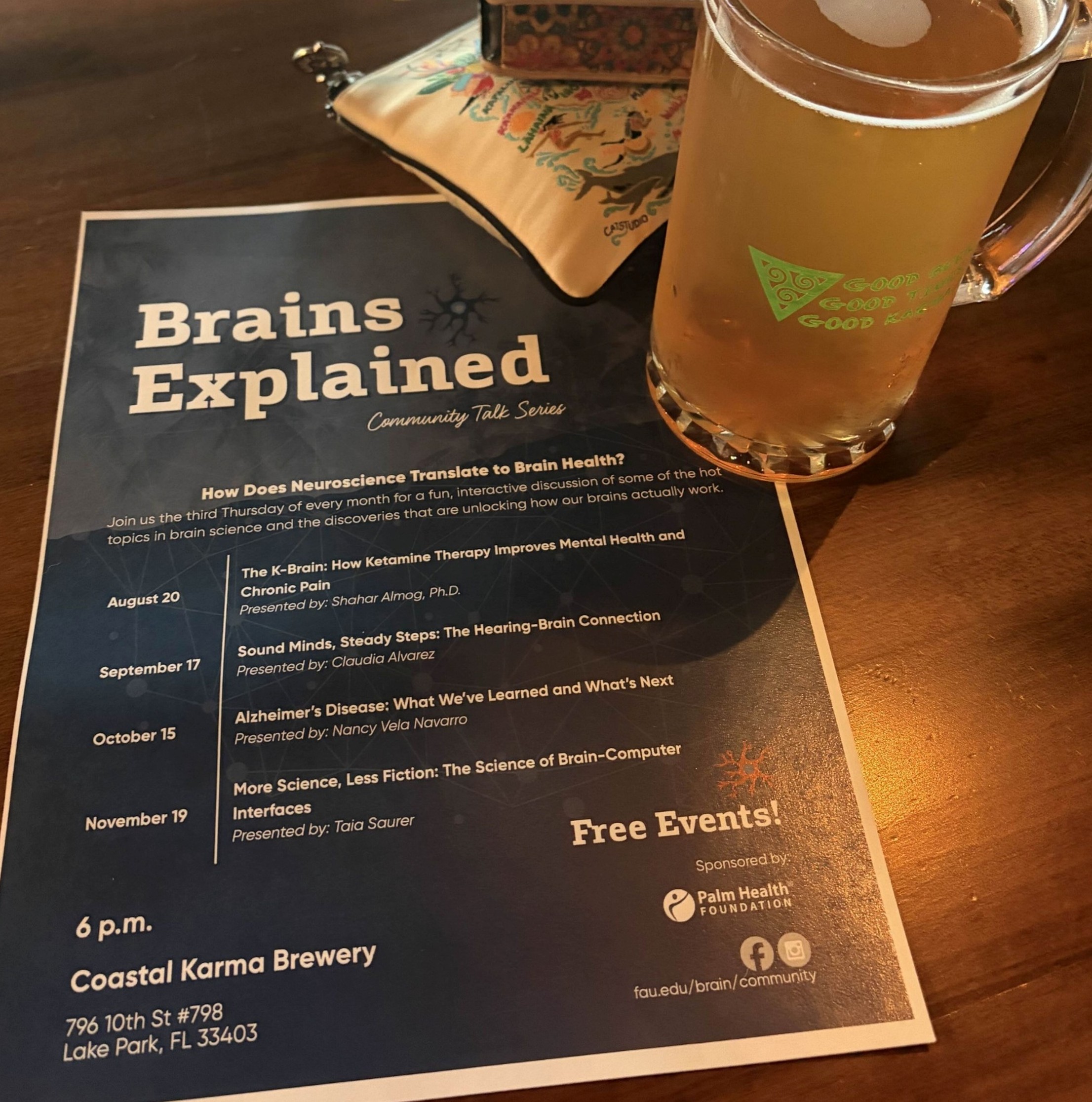 a blue flyer with dates and even descriptions on a wooden table with a full, cold pint of beer on the corner.