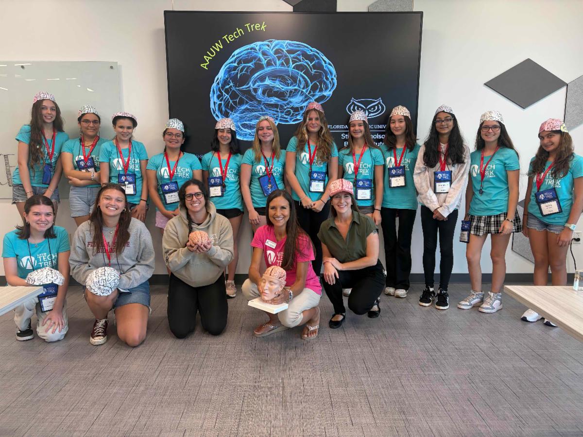 Groups of girls standing in front of a screen with a blue picture of a brain wearing caps in the shapes of brains