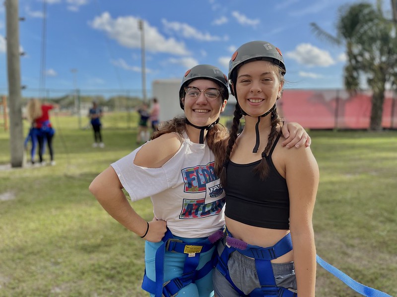 Two friends smiling while standing by the course with their helmets on
