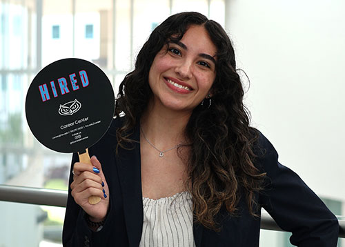 A student holding up a red shirt that says HIRE