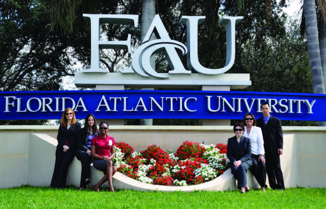 FAU staff taking a picture in front of the FAU sign