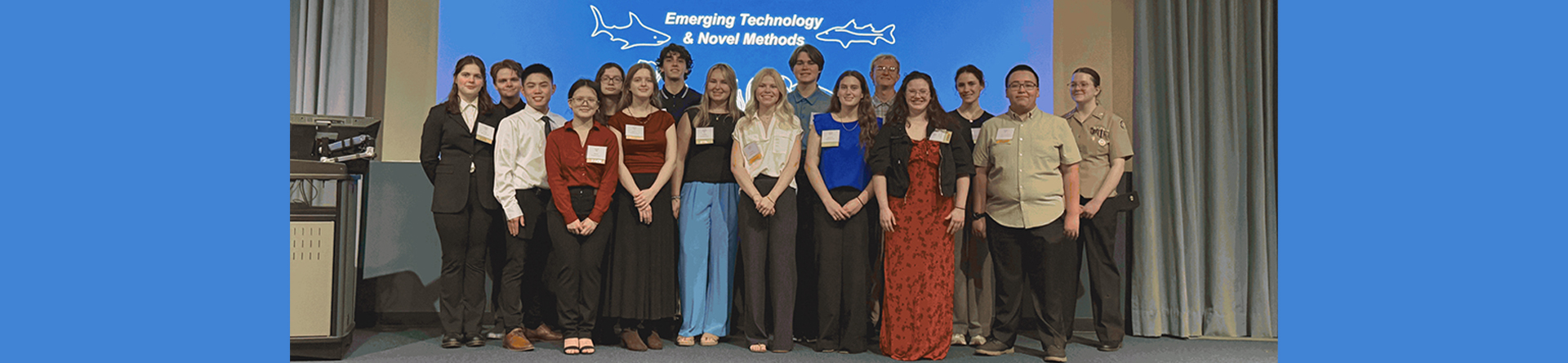 Group of students in front of blue screen with words 'IRL Symposium'