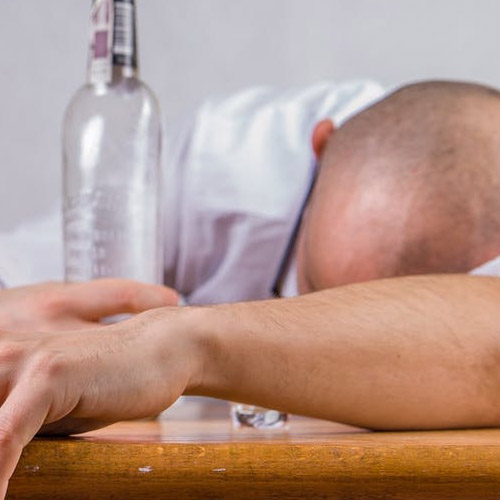 A person face down on a table with a bottle in their hand