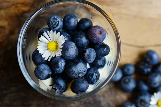 a glass bowl full of blueberries and a flower