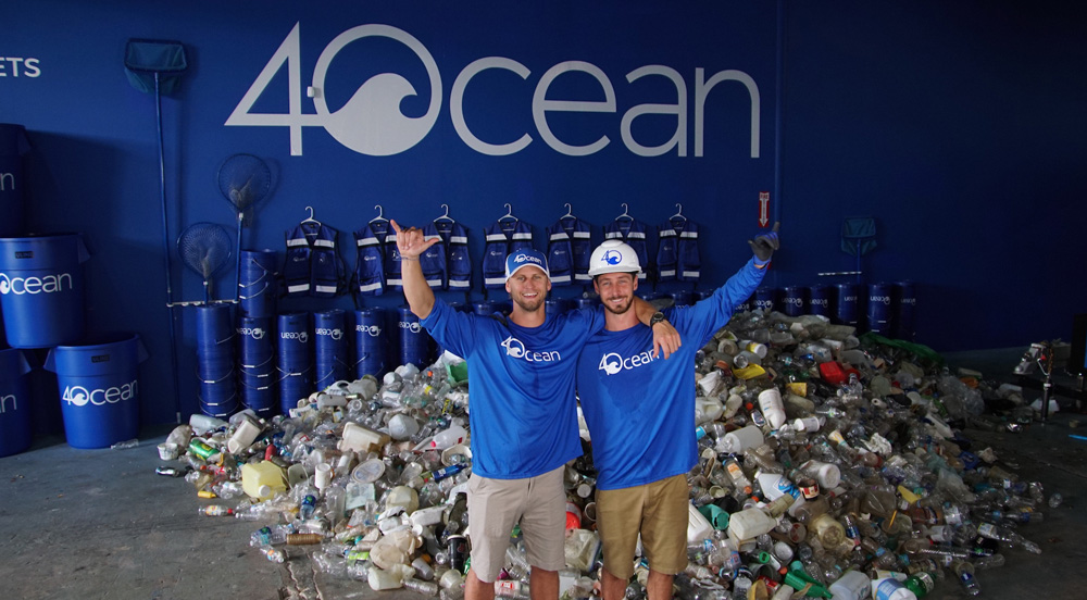 Two men staning in from of heap of garbage in a warehouse with shirts that say 4Ocean and the 4Ocean logo in the background on the wall.