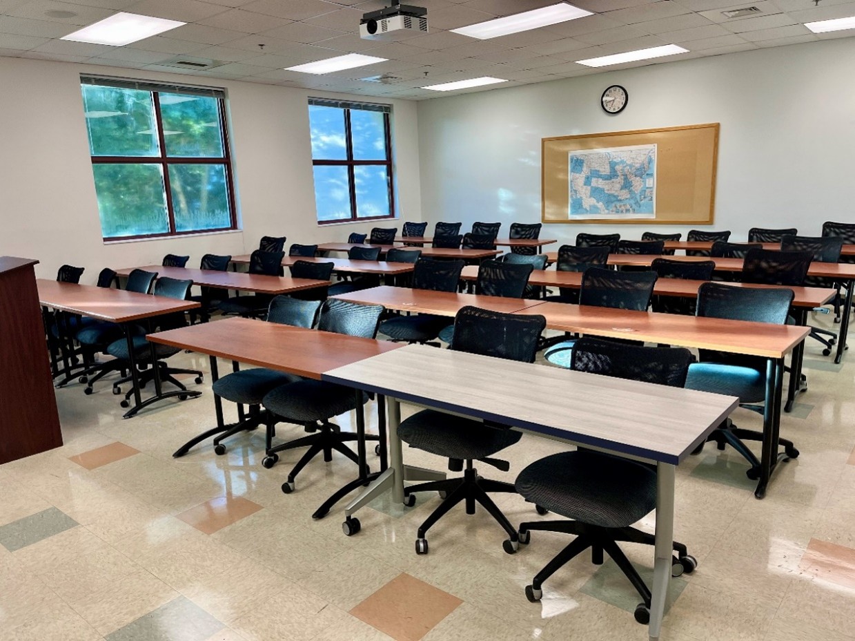 front view of classroom with brown tables and black chairs, windows, map