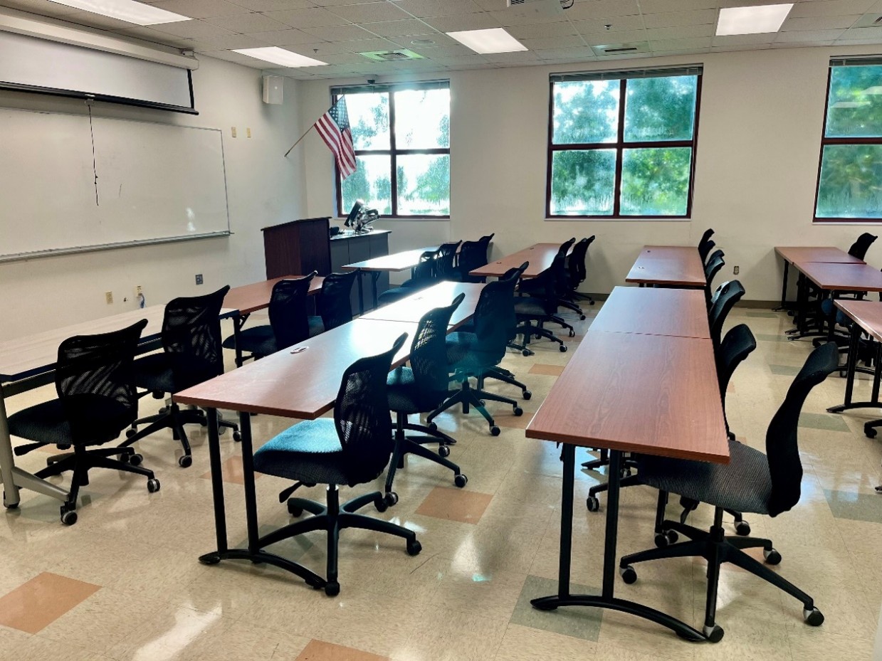 side view of classroom with brown tables and black chairs, maps, pull-down screen