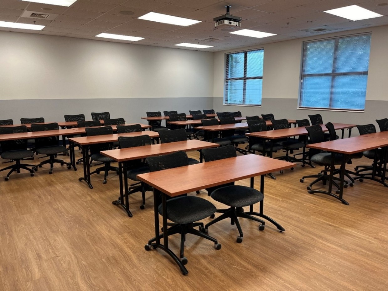front view of classroom with brown tables and black chairs, two windows