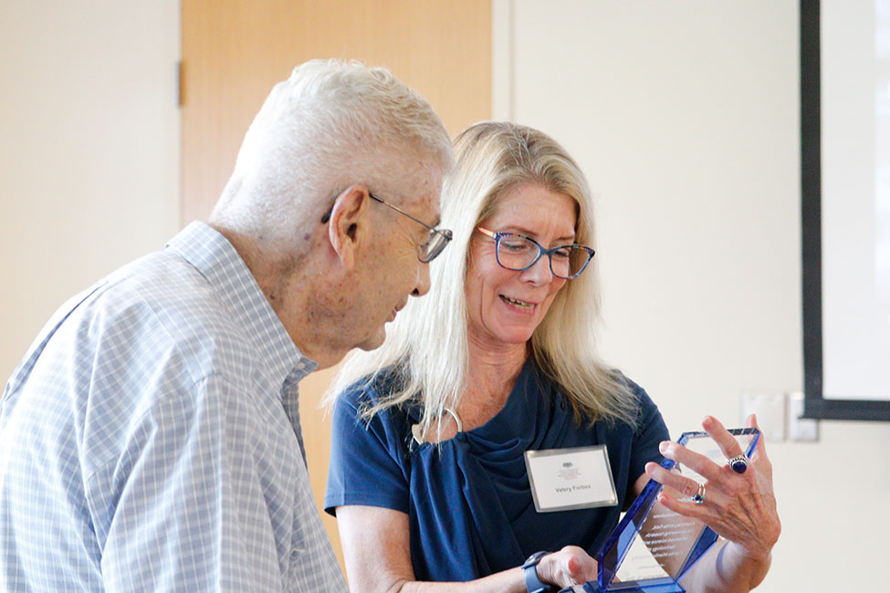 Two people stand together reading the inscription on a large, glass award.