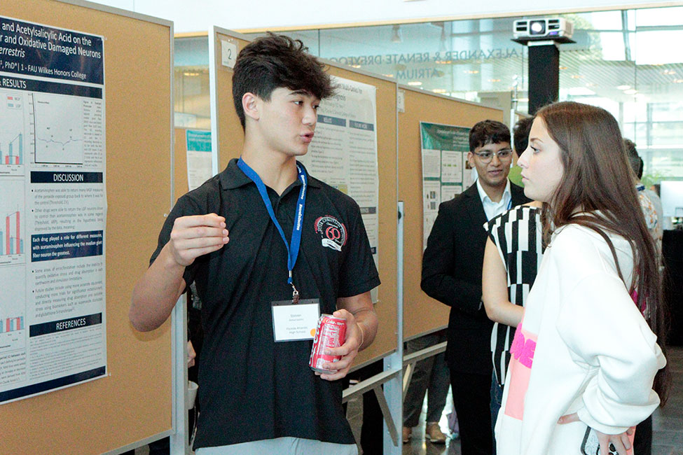 A man and a woman stand together talking in front of a research poster.