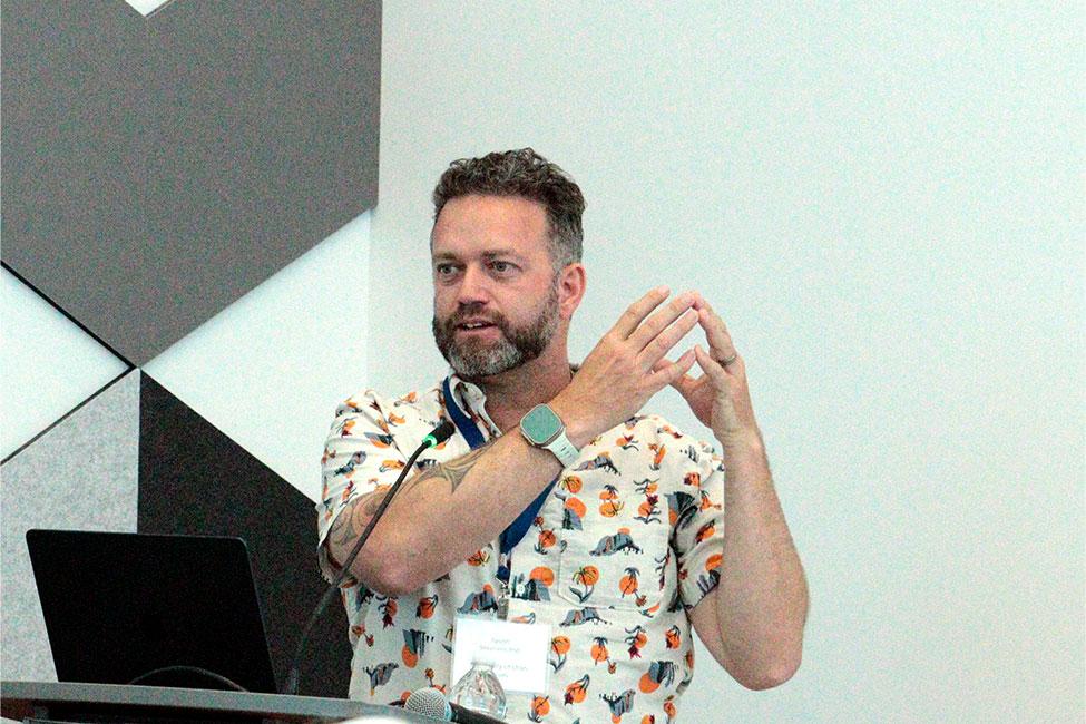A man stands at a podium, gesturing as he presents a lecture.