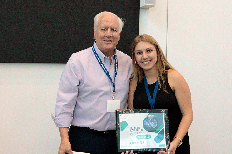 A man and woman stand side by side holding an award between them, smiling at the camera.