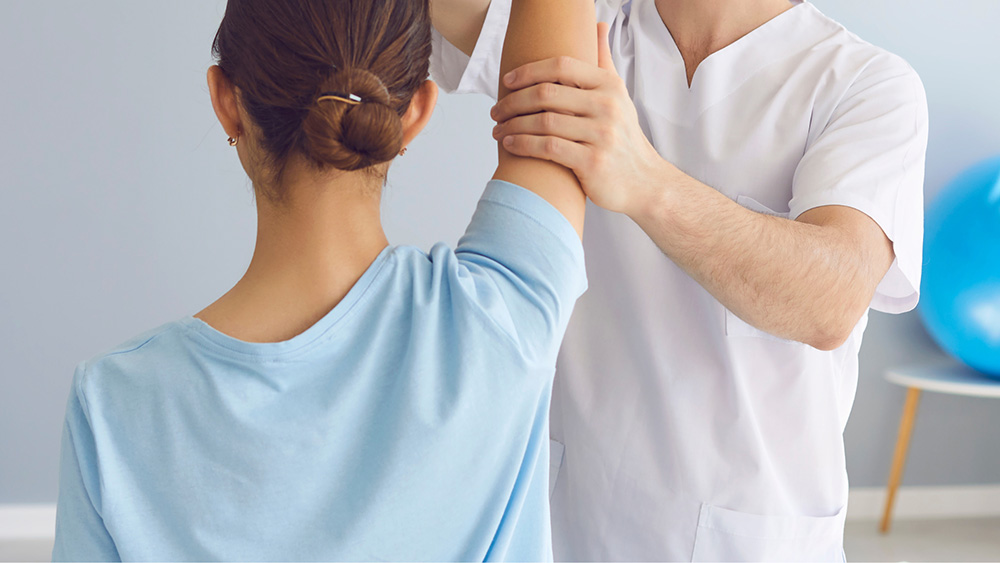 Practitioner performing an osteopathic manipulative therapy technique to improve shoulder mobility by guiding a patient’s raised arm in a clinical setting.