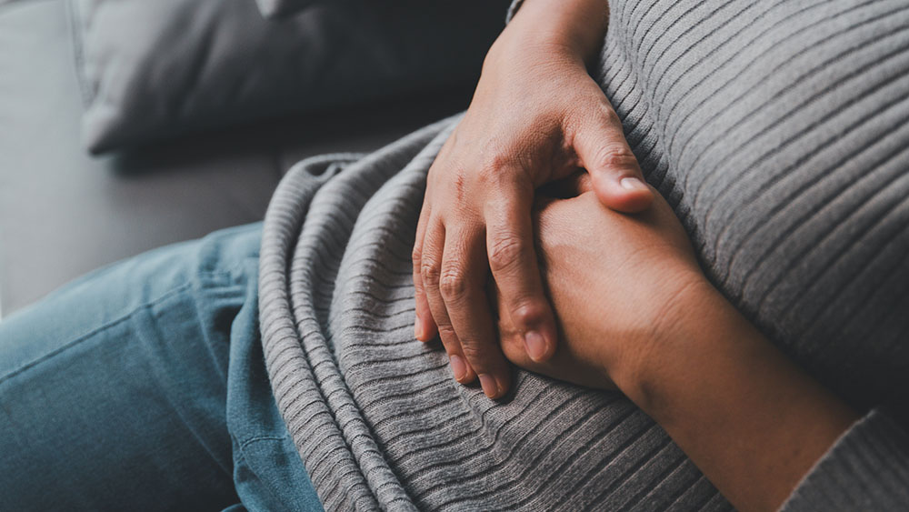 Person seated with hands resting on the abdomen, illustrating digestive discomfort or bloating.