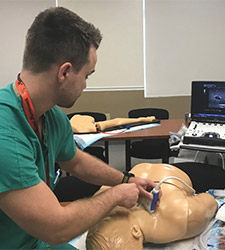 EM resident training on mannequin in emergency room setting.