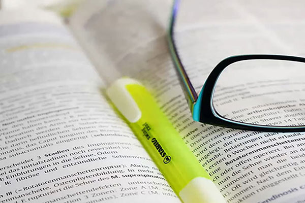 Book opened with yellow highlighter marker and reading glasses placed on top