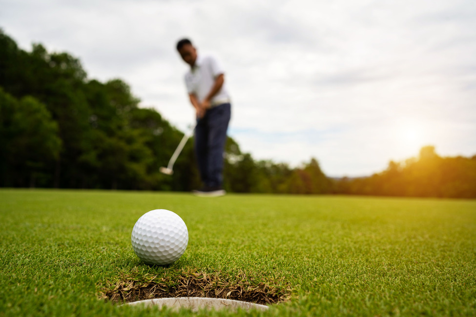 A person is on a golf course, swinging a golf club to hit a golf ball.