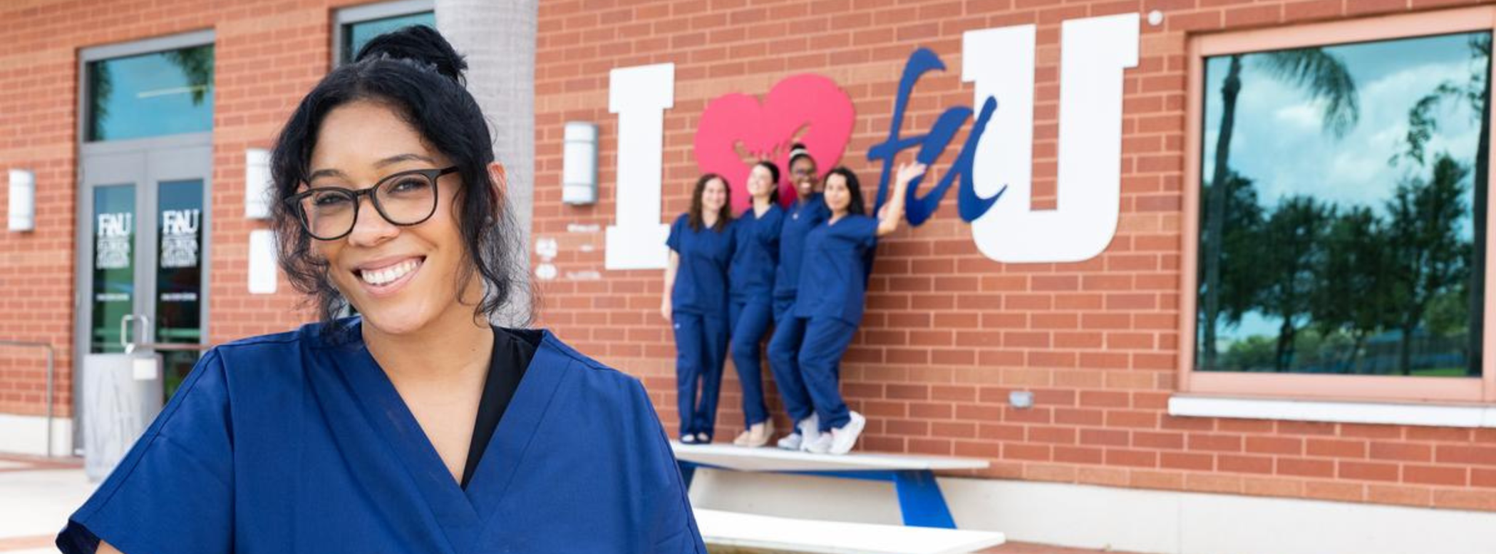 4 Nursing students wearing scrubs standing outside and smiling