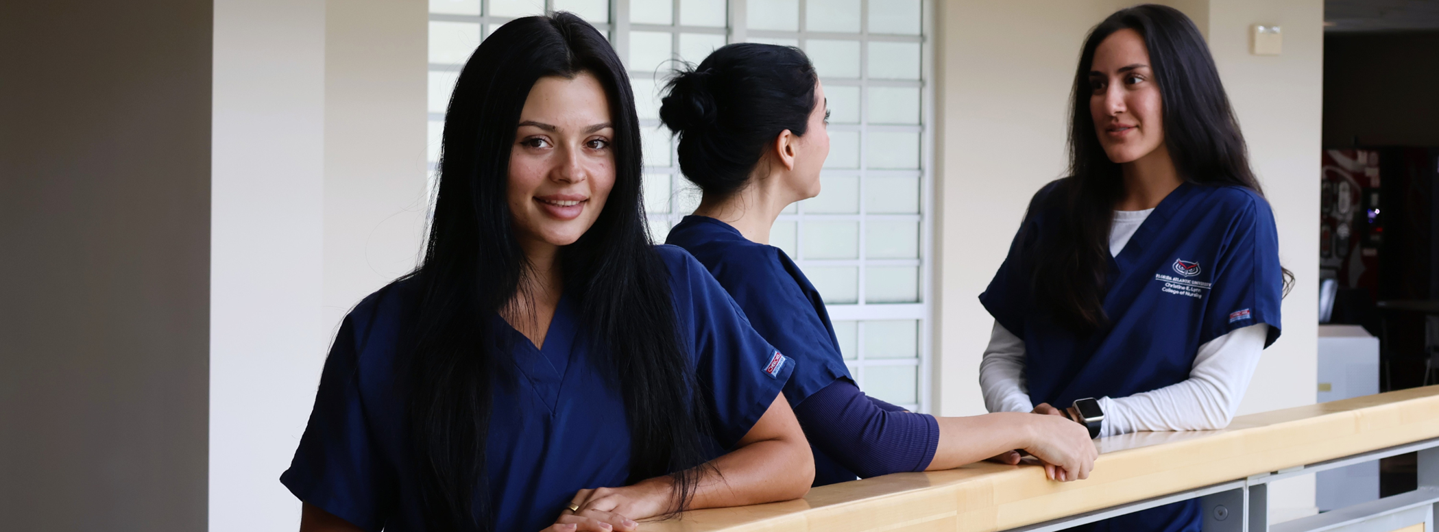 A nursing student posing for a picture with 2 students talking to each other in the background