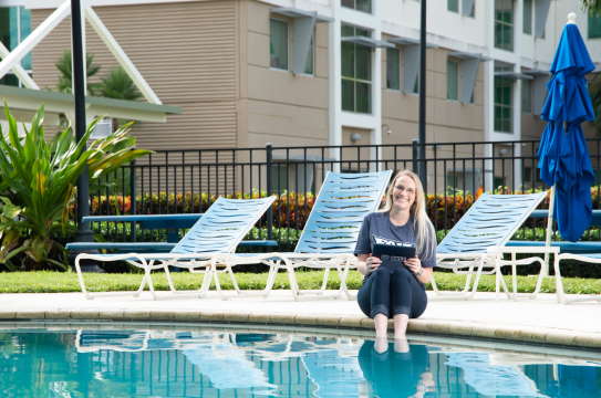 a happy student studying near a pool