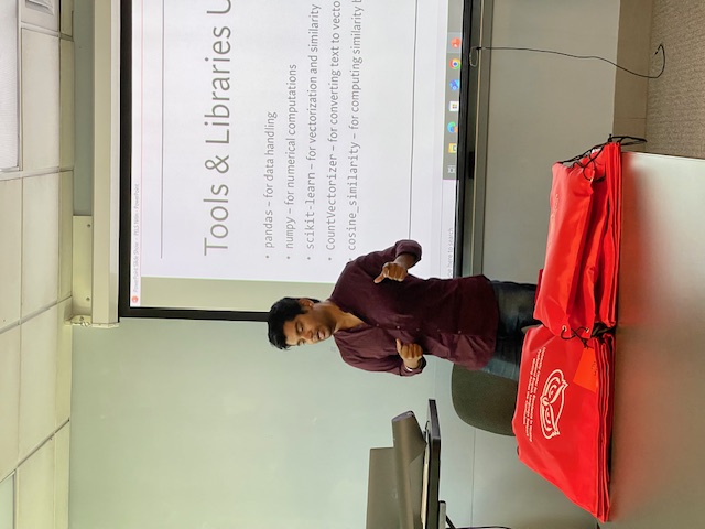 A presenter stands at a podium giving a presentation. A projection screen behind them shows slides related to vestibular rehabilitation.