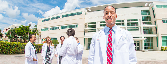 Florida Atlantic University student in white coat stands in front of the Charles E. Schmidt College of Medicine on the Boca Raton campus