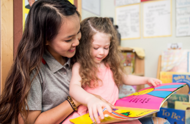 A preschool student reads a book with her teacher