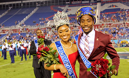 Homecoming King and Queen smiling on the football field wearing crowns