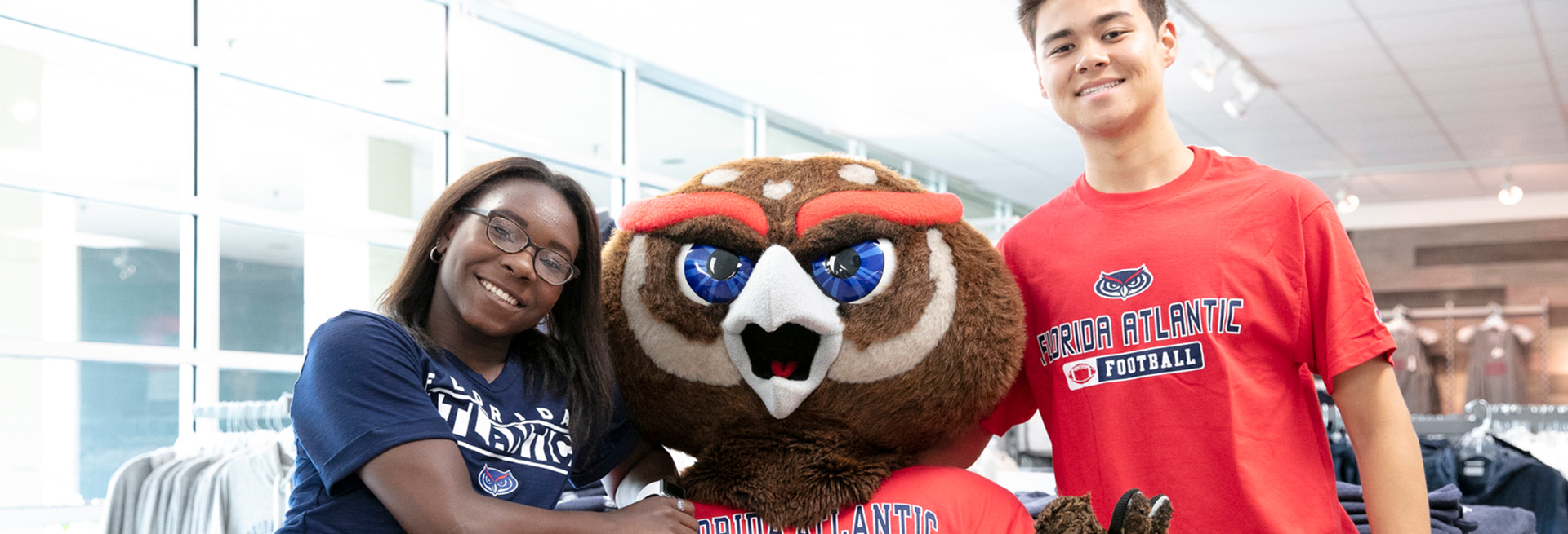 Two students next to FAU mascot Owlsley wearing FAU merchandise