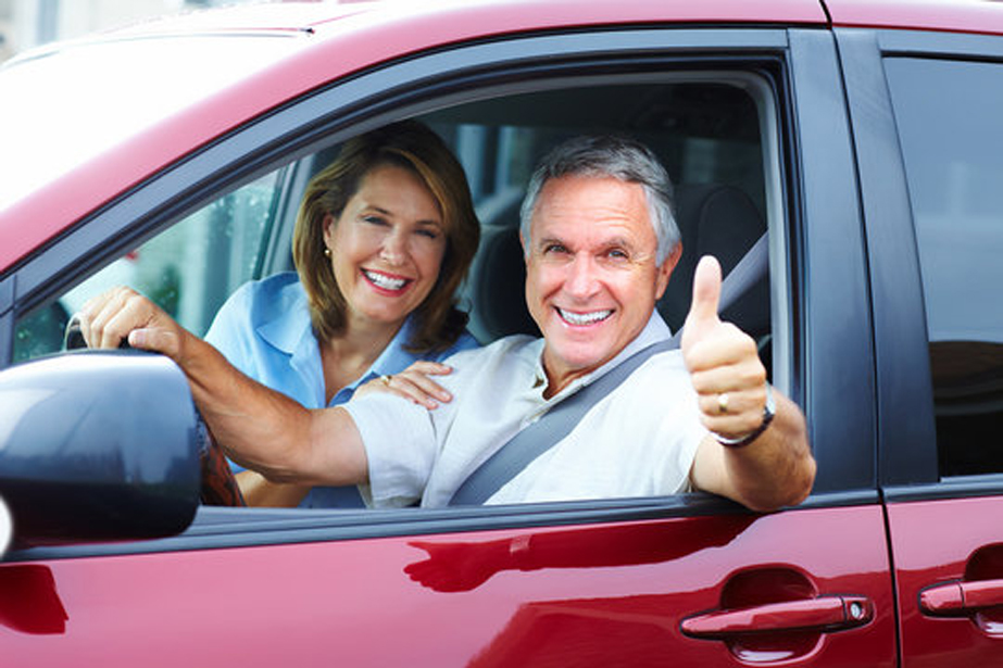 man and woman smiling looking out window of a red vehicle