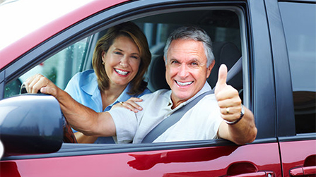 man and woman smiling and looking out window of red vehicle