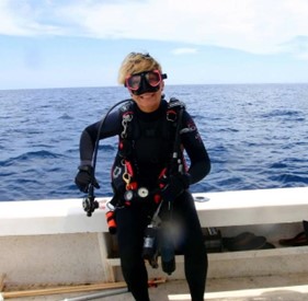 woman in scuba gear holding a fish on a boat with ocean in background