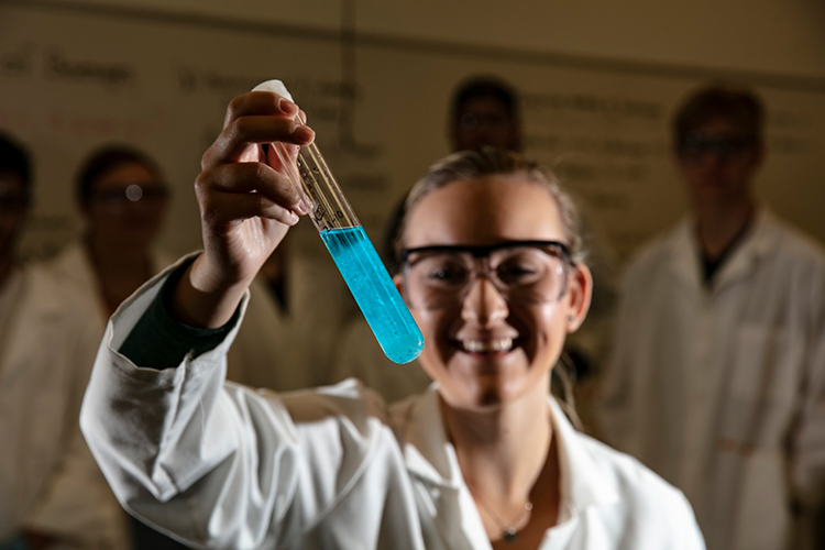 person smiling and holding test tube with blue liquid