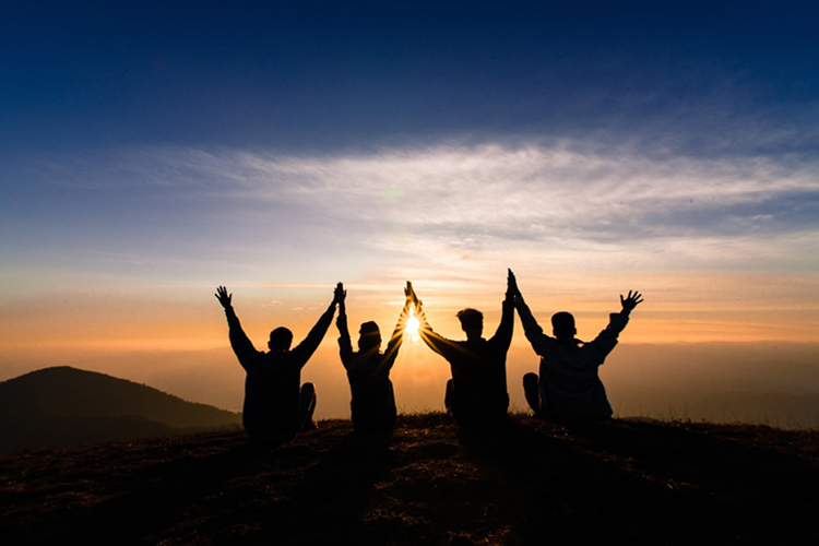 four people holding up arms with sunset background
