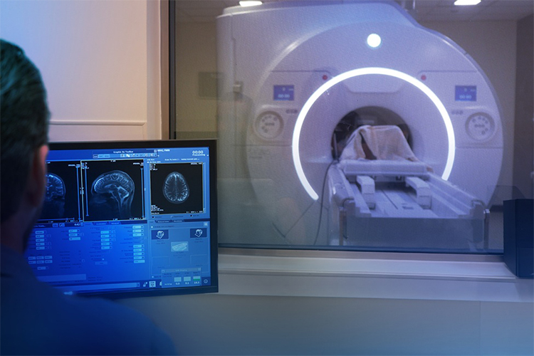 MRI machine and person looking at monitor. Photo by Alex Dolce