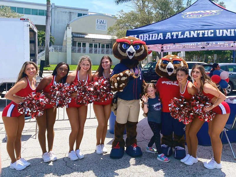 Owlsley and Hoot with cheerleaders outside next to a Florida Atlantic tent