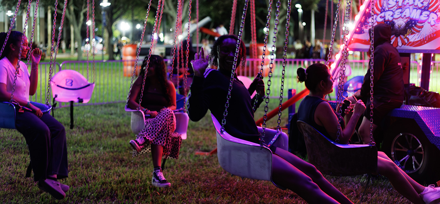 students on campus at a carnival ride sitting in swings