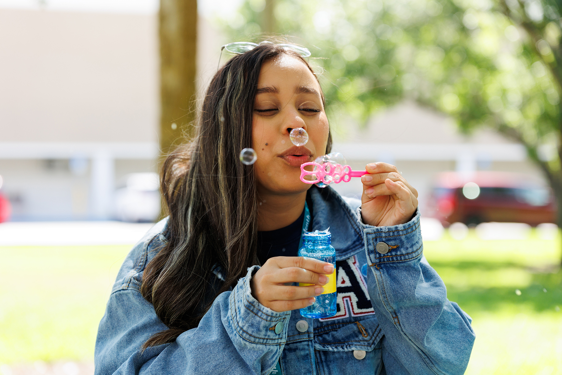 A student blowing bubbles with her eyes closed on a sunny day